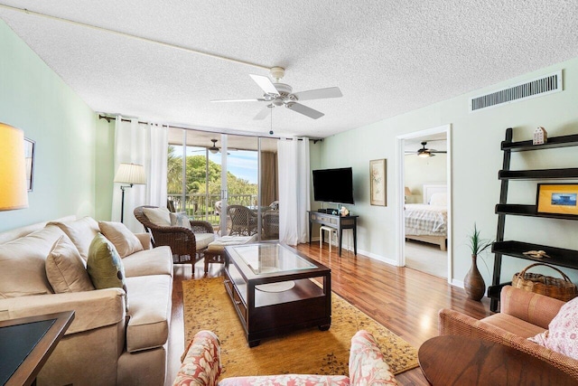 living area featuring visible vents, baseboards, wood finished floors, a textured ceiling, and a ceiling fan