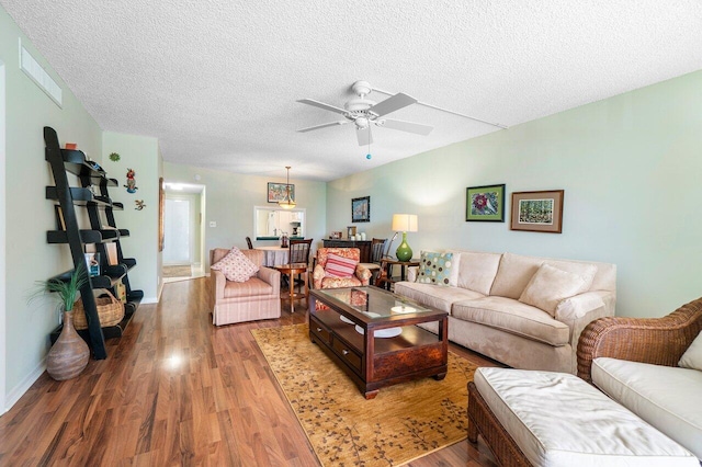 living area with visible vents, a ceiling fan, a textured ceiling, wood finished floors, and baseboards