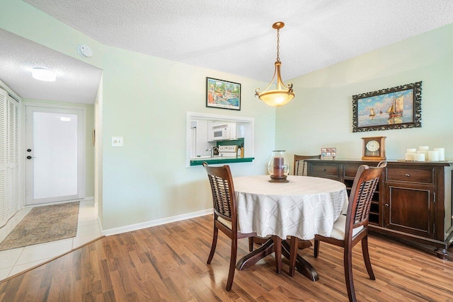 dining room with light wood-style floors, baseboards, and a textured ceiling