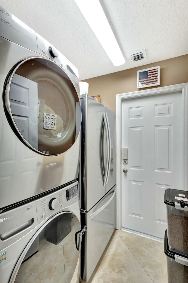 laundry room with visible vents, stacked washer and clothes dryer, a textured ceiling, light tile patterned floors, and laundry area