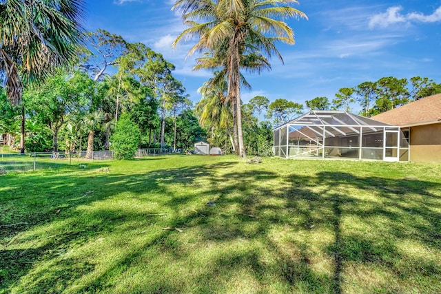 view of yard featuring glass enclosure, fence, an outdoor structure, and a shed