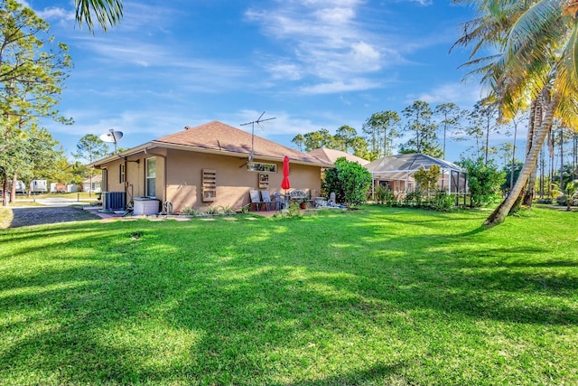 back of house featuring stucco siding, a lawn, central AC, and a lanai