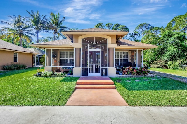 view of front of house with stucco siding, a shingled roof, a front lawn, and a sunroom