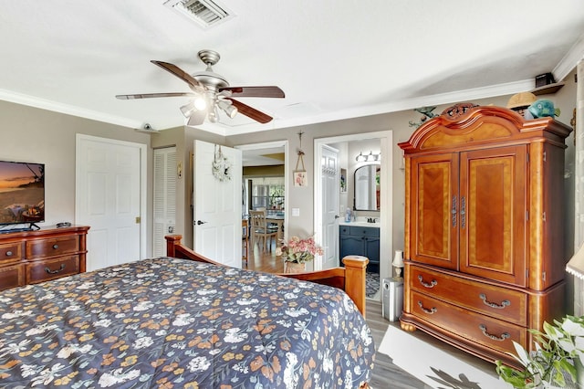 bedroom with wood finished floors, visible vents, a sink, crown molding, and connected bathroom