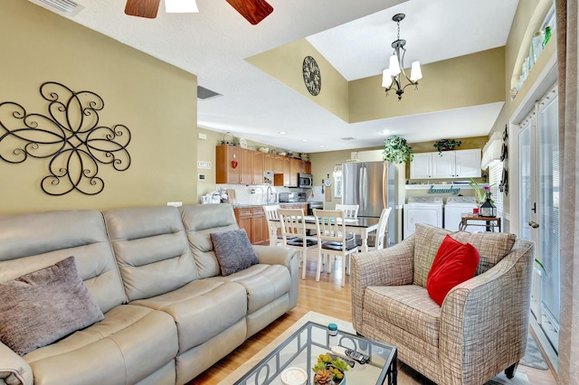 living area featuring washer and clothes dryer, visible vents, ceiling fan with notable chandelier, and light wood finished floors