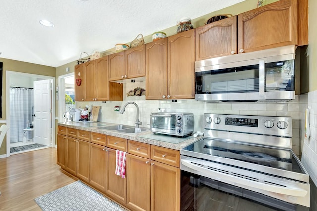 kitchen featuring a toaster, light countertops, decorative backsplash, stainless steel appliances, and a sink