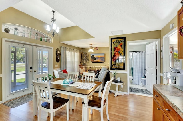 dining space featuring light wood finished floors, ceiling fan with notable chandelier, french doors, and a textured ceiling