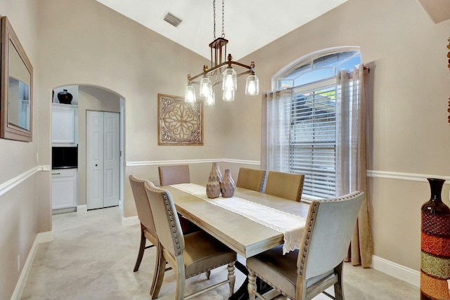 dining area with arched walkways, visible vents, baseboards, and vaulted ceiling