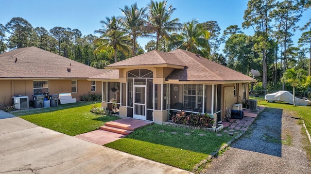 view of front of property featuring stucco siding, central AC unit, a front yard, and a sunroom