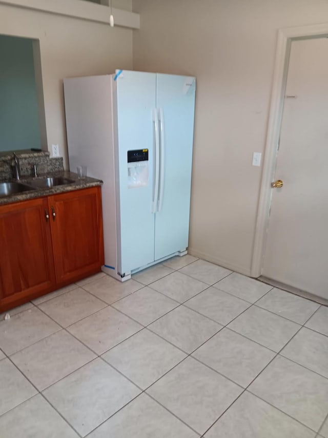 5489 NW Evanston Ave, Port Saint Lucie, FL 34983 - kitchen featuring white refrigerator with ice dispenser, a sink, brown cabinets, light tile patterned floors, and dark stone countertops