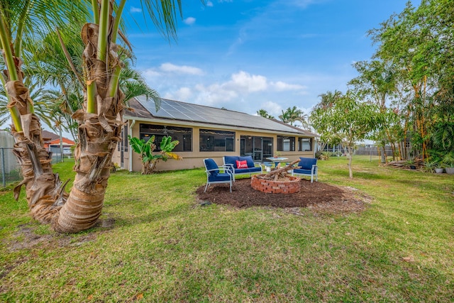 back of house featuring fence, an outdoor fire pit, stucco siding, a lawn, and roof mounted solar panels