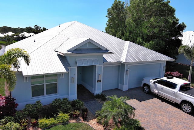 view of front facade with stucco siding, decorative driveway, a garage, and metal roof