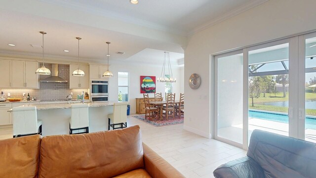 kitchen featuring tasteful backsplash, crown molding, wall chimney range hood, double oven, and pendant lighting