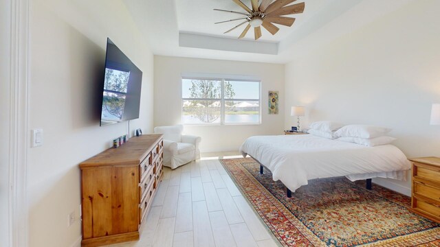 bedroom featuring a raised ceiling, light wood-style floors, and ceiling fan