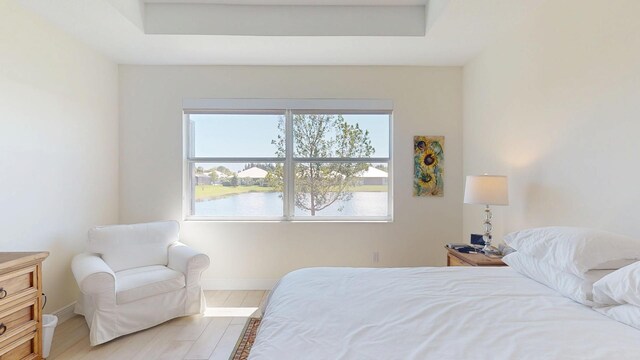 bedroom with a tray ceiling, light wood-style flooring, and baseboards