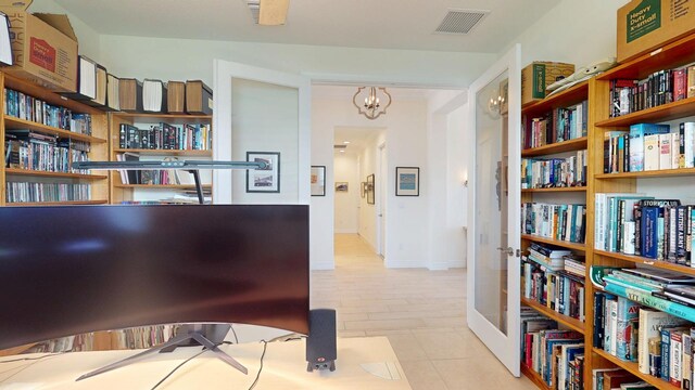 office with light tile patterned flooring, visible vents, an inviting chandelier, and wall of books