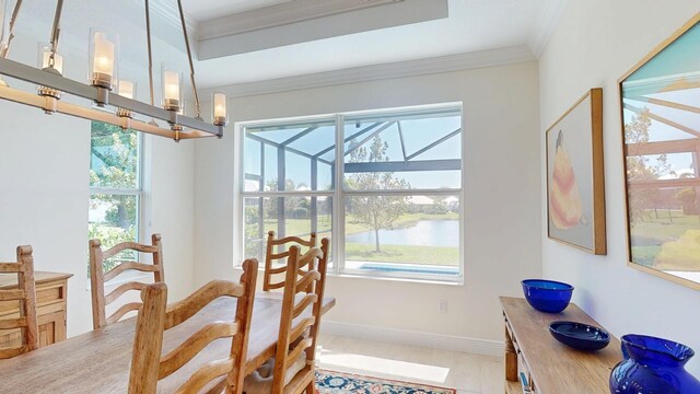 dining room with baseboards, a sunroom, ornamental molding, a water view, and a chandelier