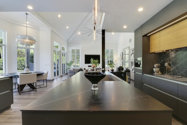 kitchen with decorative backsplash, a large island with sink, light wood-style flooring, an inviting chandelier, and modern cabinets