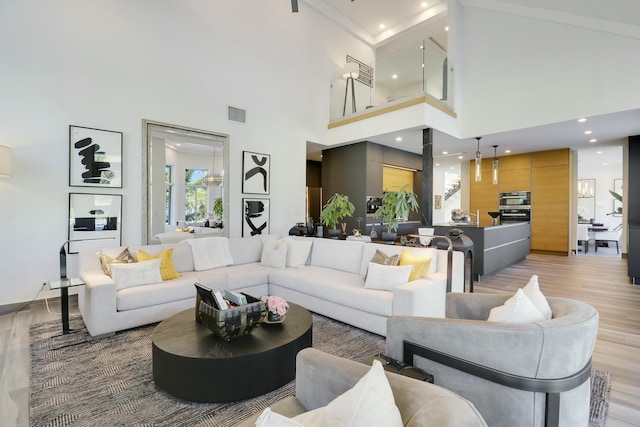 living room with recessed lighting, light wood-style floors, visible vents, and a towering ceiling