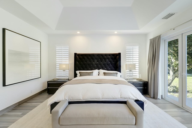 bedroom with access to exterior, visible vents, light wood-type flooring, and a raised ceiling