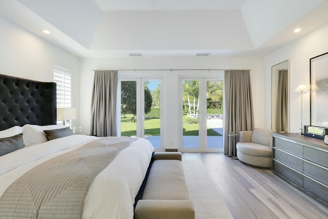 bedroom featuring access to exterior, visible vents, a tray ceiling, and wood finished floors