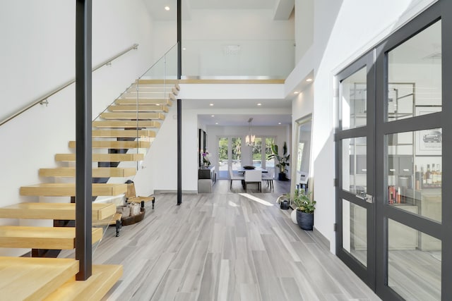 entryway featuring stairs, light wood-style flooring, french doors, and a towering ceiling