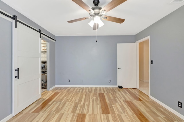 unfurnished bedroom with light wood-style flooring, baseboards, a barn door, and ceiling fan