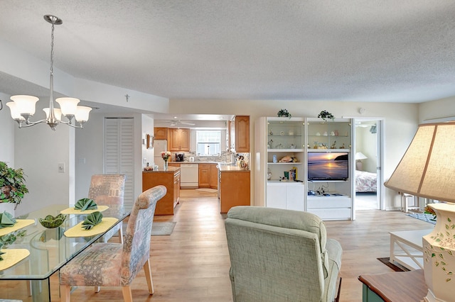 living room featuring a textured ceiling, light wood-style flooring, and ceiling fan with notable chandelier