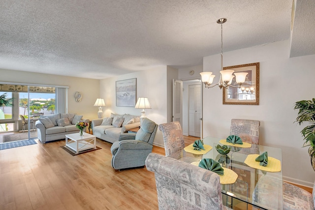 living area with baseboards, a textured ceiling, light wood-type flooring, and an inviting chandelier