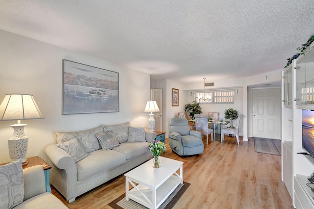 living room with visible vents, light wood-style flooring, and a textured ceiling