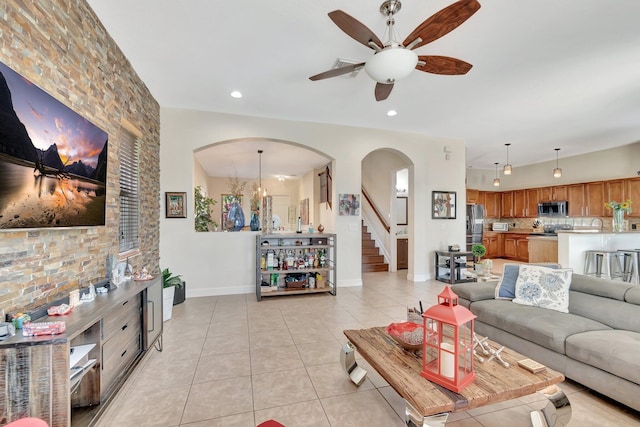 living area featuring light tile patterned floors, visible vents, arched walkways, stairs, and ceiling fan with notable chandelier