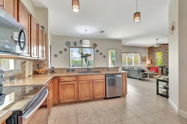 kitchen featuring backsplash, appliances with stainless steel finishes, a peninsula, brown cabinetry, and a sink