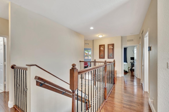 hall featuring an upstairs landing, visible vents, baseboards, and wood finished floors