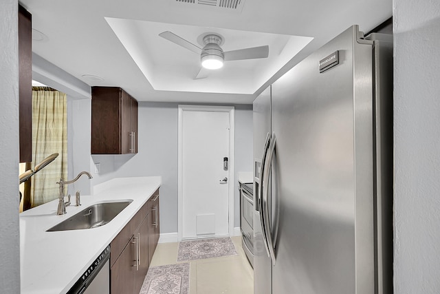 kitchen featuring ceiling fan, a sink, a raised ceiling, light countertops, and appliances with stainless steel finishes