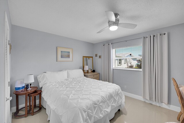 bedroom with light tile patterned flooring, a textured ceiling, baseboards, and a ceiling fan