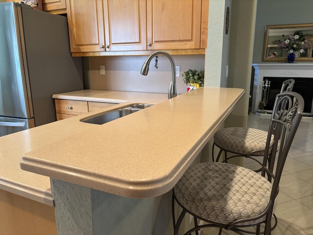 kitchen featuring a breakfast bar, a sink, freestanding refrigerator, light countertops, and light tile patterned floors