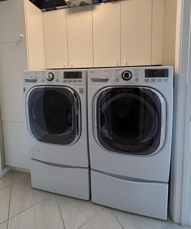 clothes washing area with cabinet space, washing machine and dryer, and light tile patterned flooring