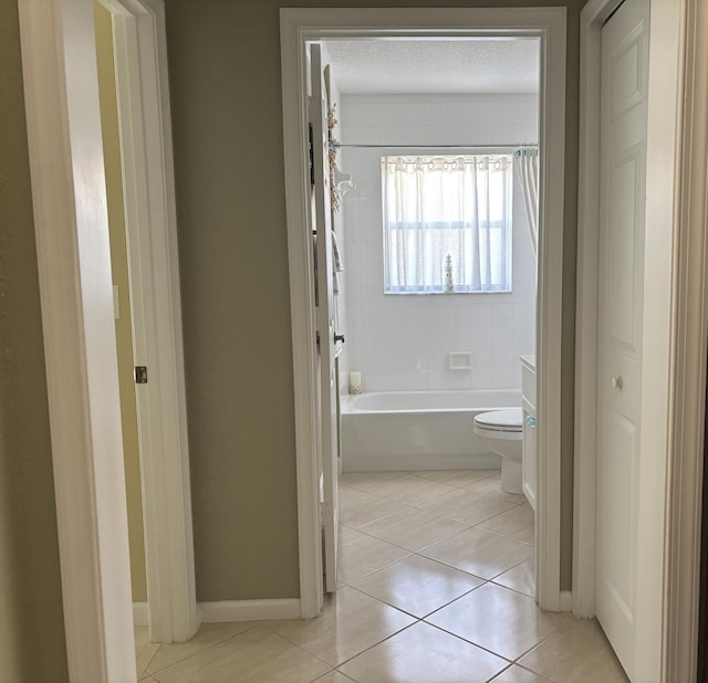 bathroom featuring toilet, a textured ceiling,  shower combination, tile patterned flooring, and baseboards