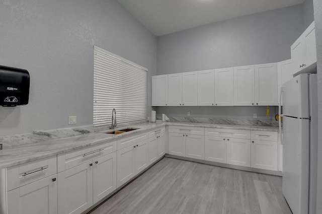 kitchen featuring a sink, light stone counters, freestanding refrigerator, white cabinets, and light wood finished floors