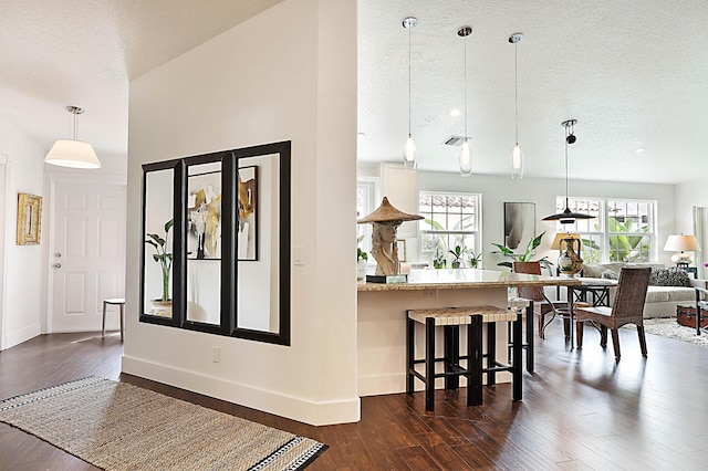 interior space featuring a breakfast bar, dark wood-style flooring, a wealth of natural light, and a textured ceiling