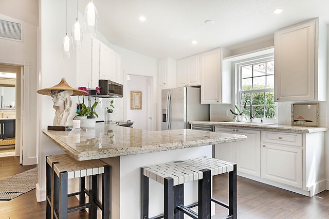 kitchen featuring a kitchen bar, visible vents, a sink, dark wood-style floors, and appliances with stainless steel finishes