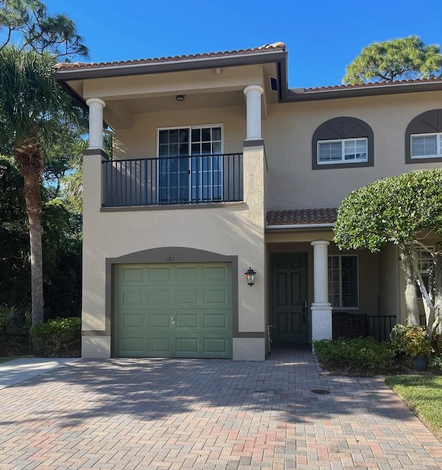 mediterranean / spanish-style house featuring a balcony, an attached garage, stucco siding, a tile roof, and decorative driveway