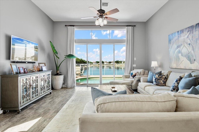 living room featuring visible vents, a water view, wood finished floors, and a ceiling fan