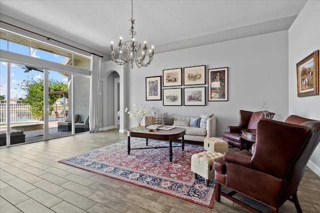 living area with arched walkways, a chandelier, a textured ceiling, and baseboards