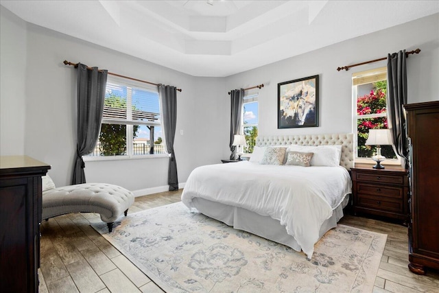 bedroom featuring a raised ceiling, baseboards, and light wood finished floors