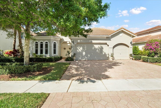 mediterranean / spanish-style house featuring stucco siding, decorative driveway, a garage, and a tiled roof