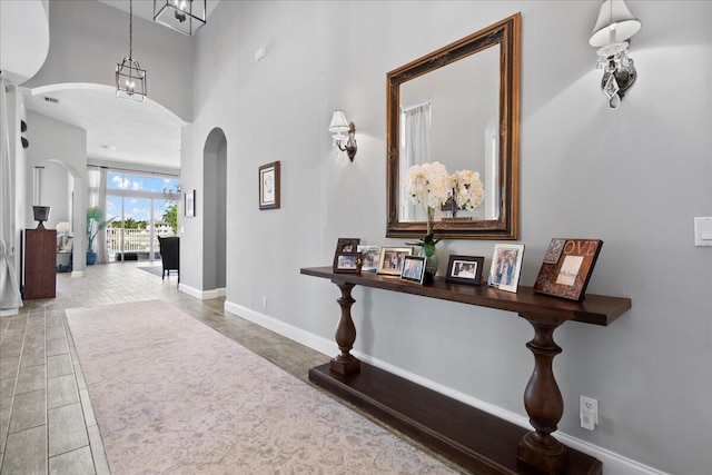 corridor featuring arched walkways, a high ceiling, and baseboards