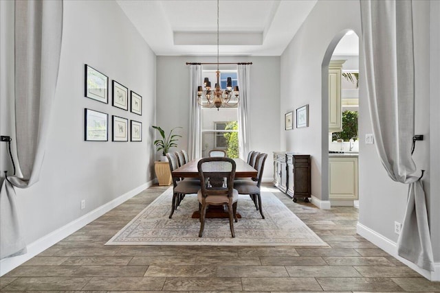 dining space with a tray ceiling, baseboards, a chandelier, and wood finish floors