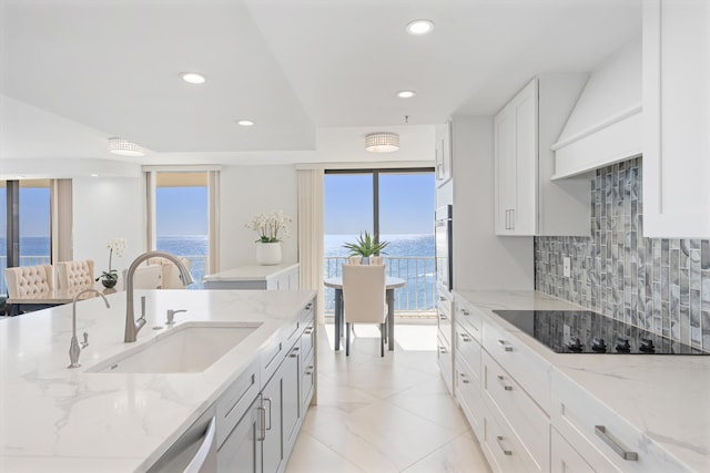 kitchen featuring light stone countertops, plenty of natural light, a sink, decorative backsplash, and black electric cooktop