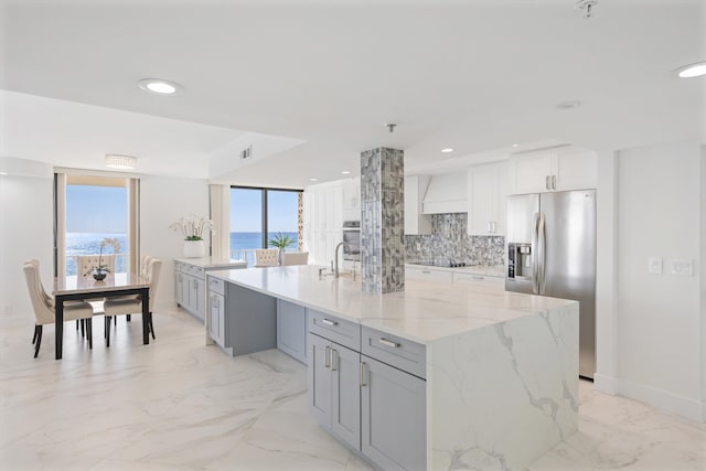 kitchen with light stone countertops, gray cabinets, stainless steel refrigerator with ice dispenser, marble finish floor, and tasteful backsplash